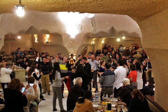 Image description: A lively Turkish Night at a cave restaurant in Cappadocia. People are enjoying a delicious dinner and drinks while being entertained by traditional Turkish music and dance performances.